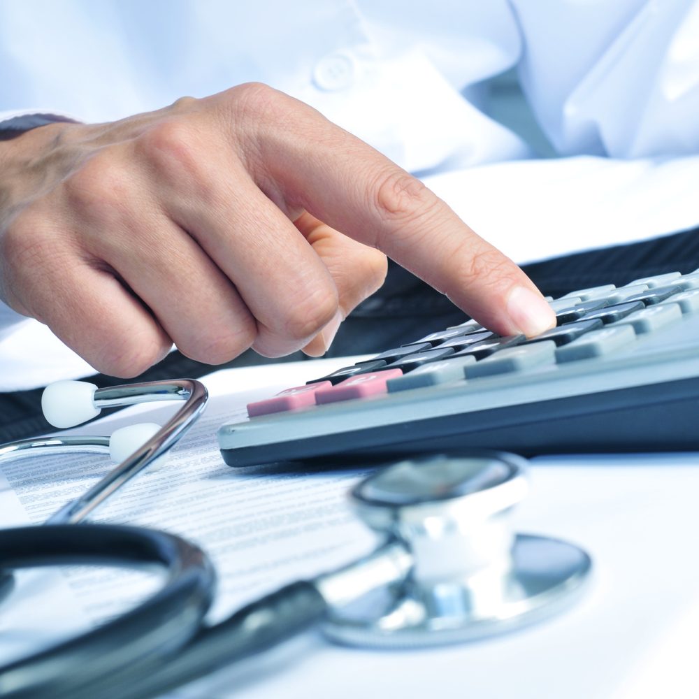 closeup of a young caucasian healthcare professional wearing a white coat calculates on an electronic calculator